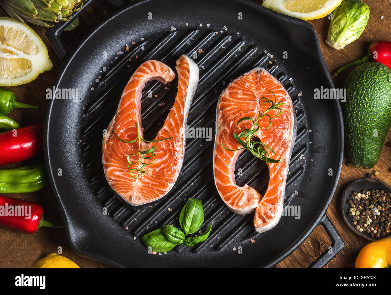 Ingredientes para cocinar la cena. Dos piezas de materias crudas y Salmón  con verduras, hierbas, limón, aguacate, alcachofas, especias, en plancha de  asar en cacerola de fondo de madera Fotografía de stock -