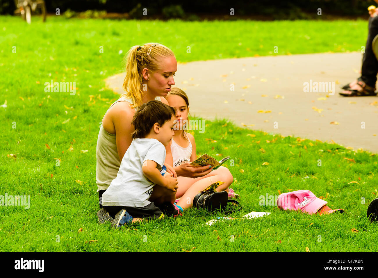 En Goteborg, Suecia - 25 de julio de 2016: adulto joven mujer leyendo un libro pequeño para dos niños en un parque público. La gente real en cada Foto de stock