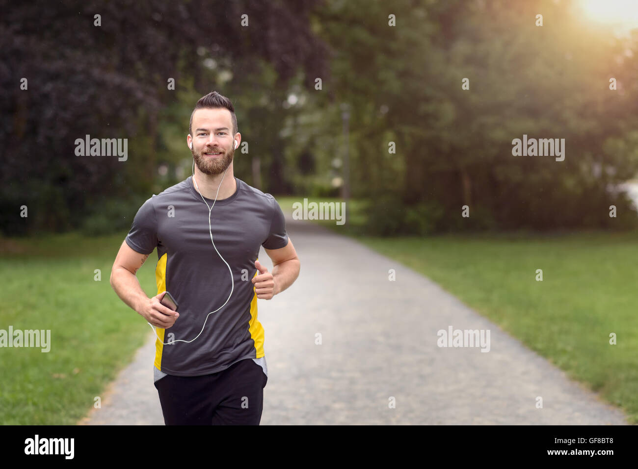 Colocar joven barbudo correr por un parque escuchando música en su teléfono móvil, acercando a la parte superior del cuerpo de la cámara con copia Foto de stock