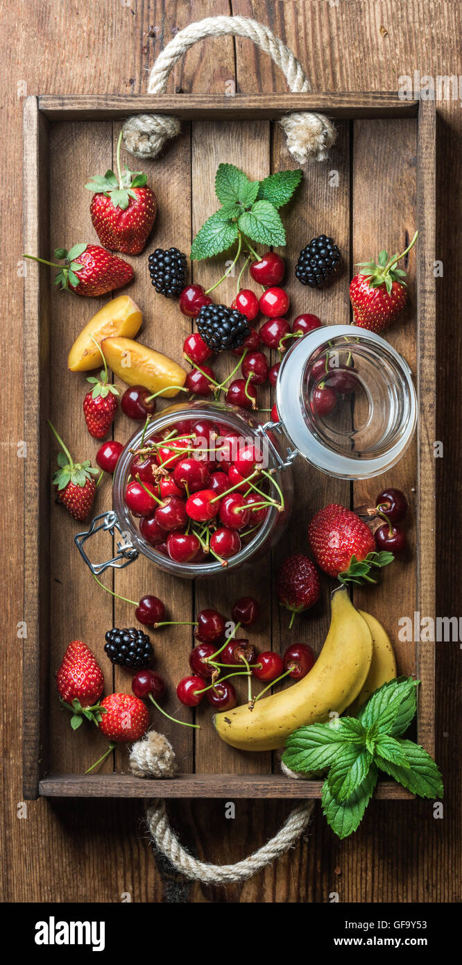 Buena variedad de fruta de verano. Cerezas dulces, fresas, moras, melocotones, plátanos y hojas de menta Foto de stock