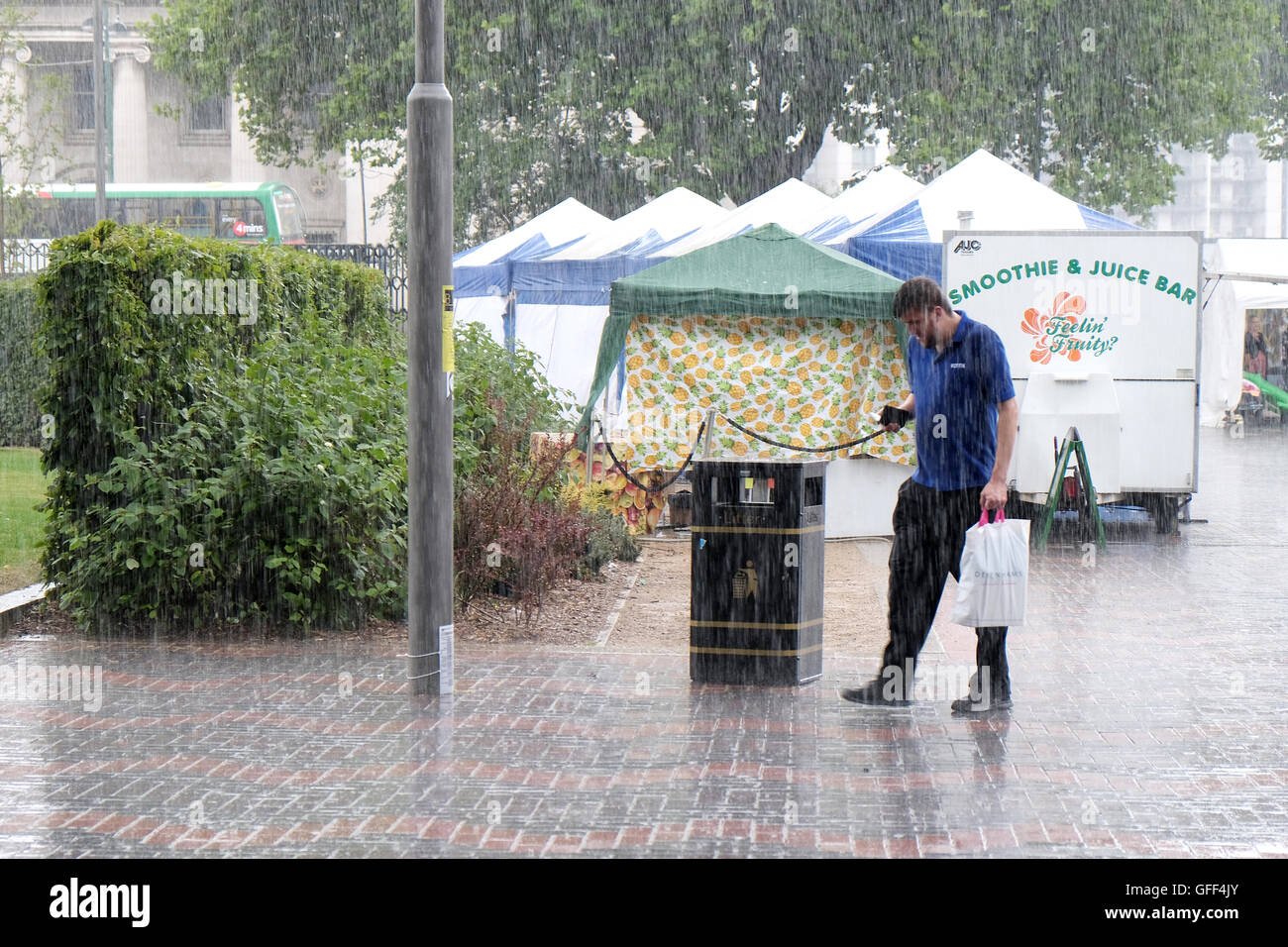 Un macho shopper cruza una zona peatonal en la lluvia torrencial tras haber sido atrapados por una repentina tormenta de verano bu Foto de stock