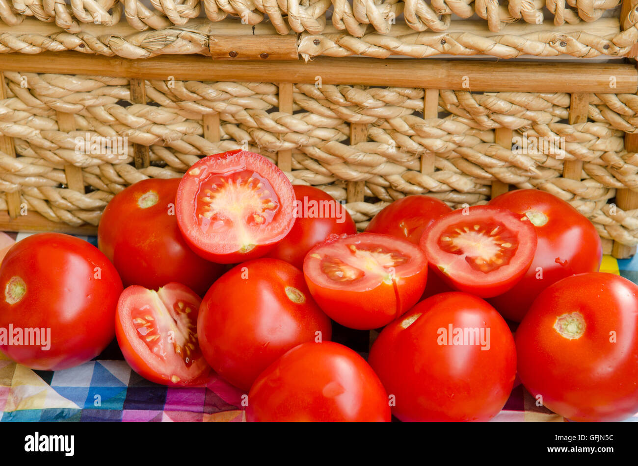 Todo y cortar los tomates apilados contra una cesta tejida Foto de stock