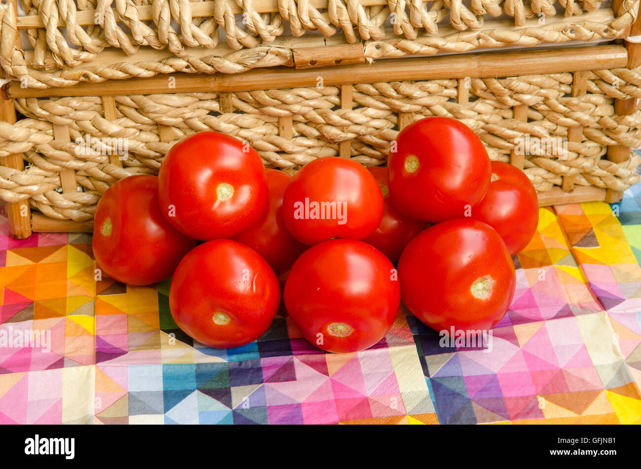 Los tomates apilados contra una cesta tejida Foto de stock