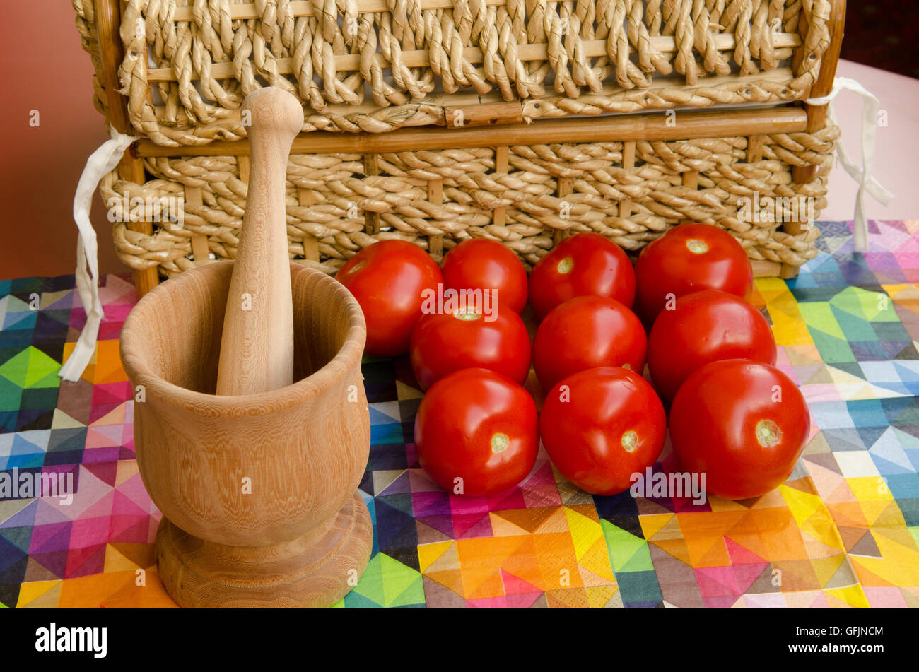 Los tomates apilados contra una cesta tejida con mortero de madera Foto de stock