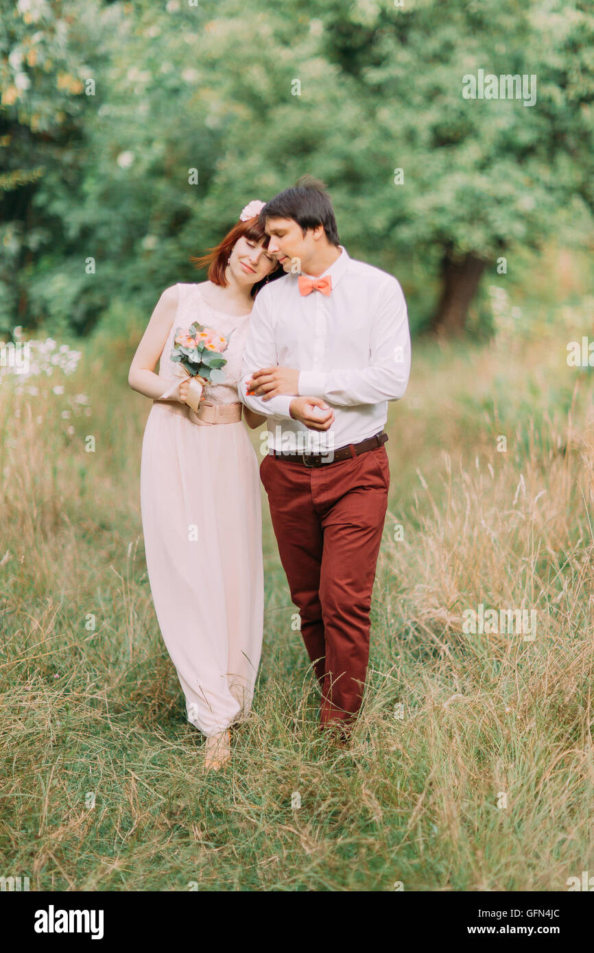 Recién casados hipster amorosa pareja vestidos de boda vestido y traje de  campo verde en el bosque en día soleado Fotografía de stock - Alamy