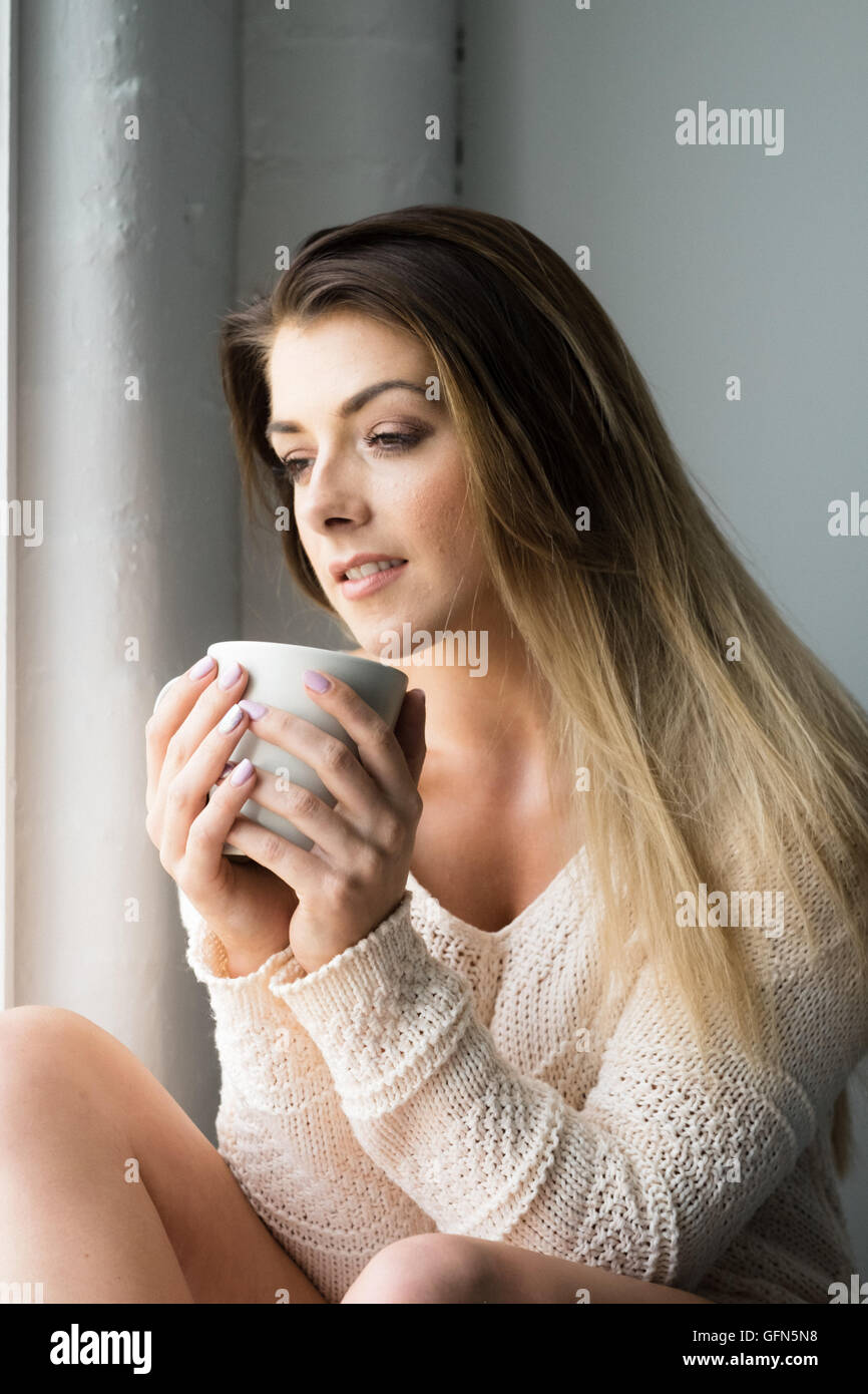 Mujer sonriente en su 20s disfrutar de una relajante bebida Foto de stock