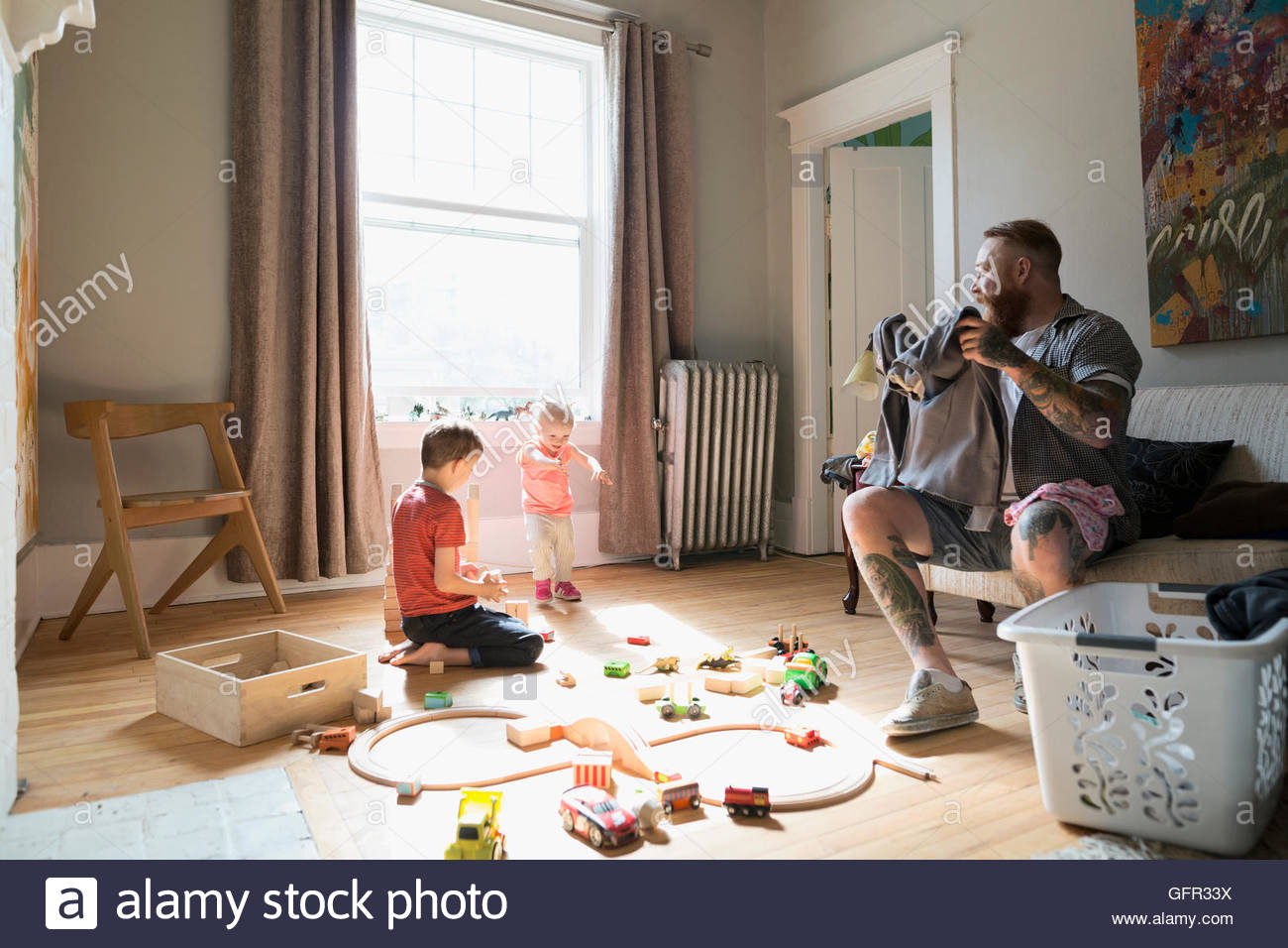 Padre plegado cerca de lavandería niños jugando con tren de juguete y bloques de madera Foto de stock