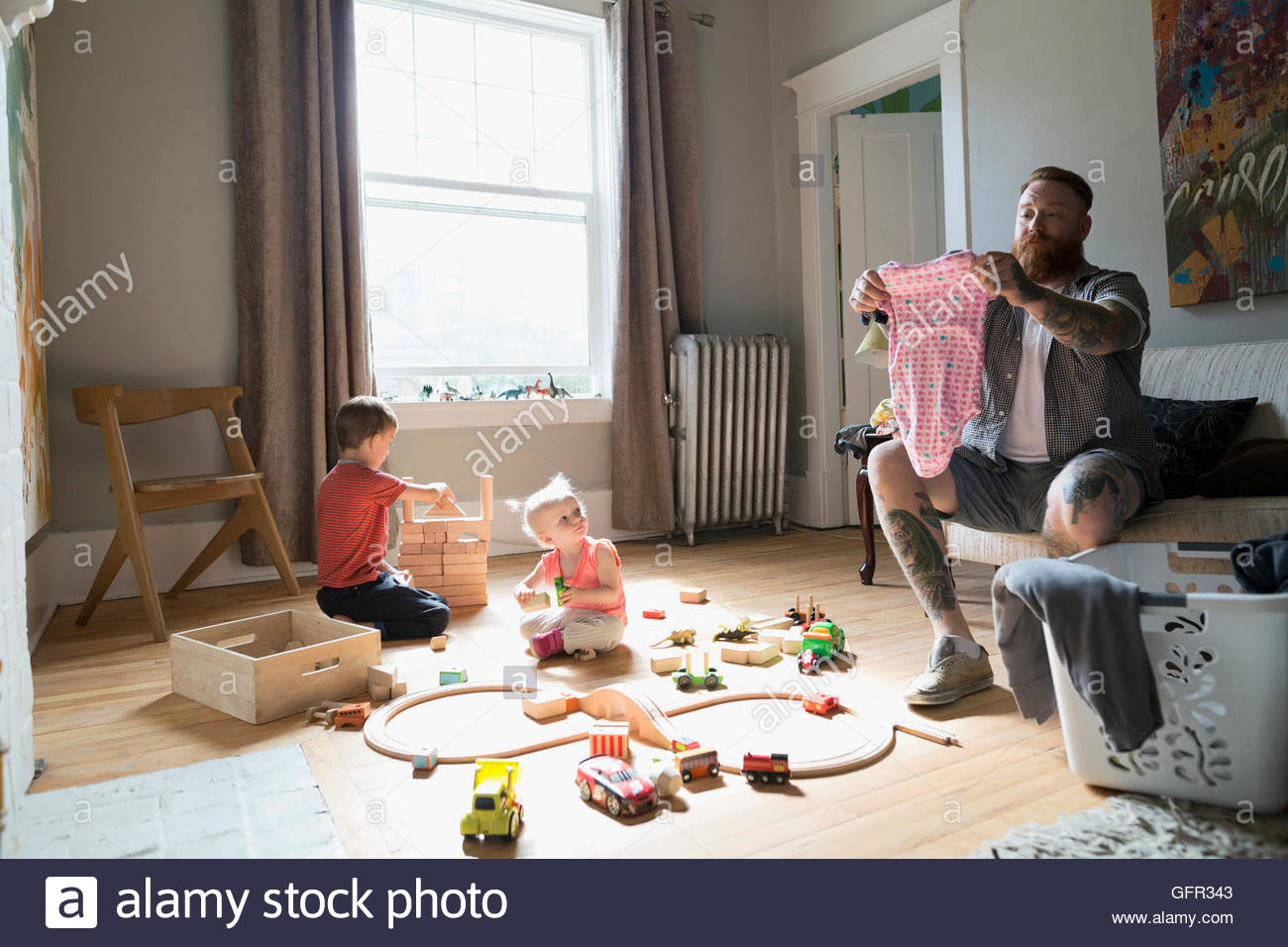 Padre plegado cerca de lavandería niños jugando con tren de juguete y bloques de madera Foto de stock
