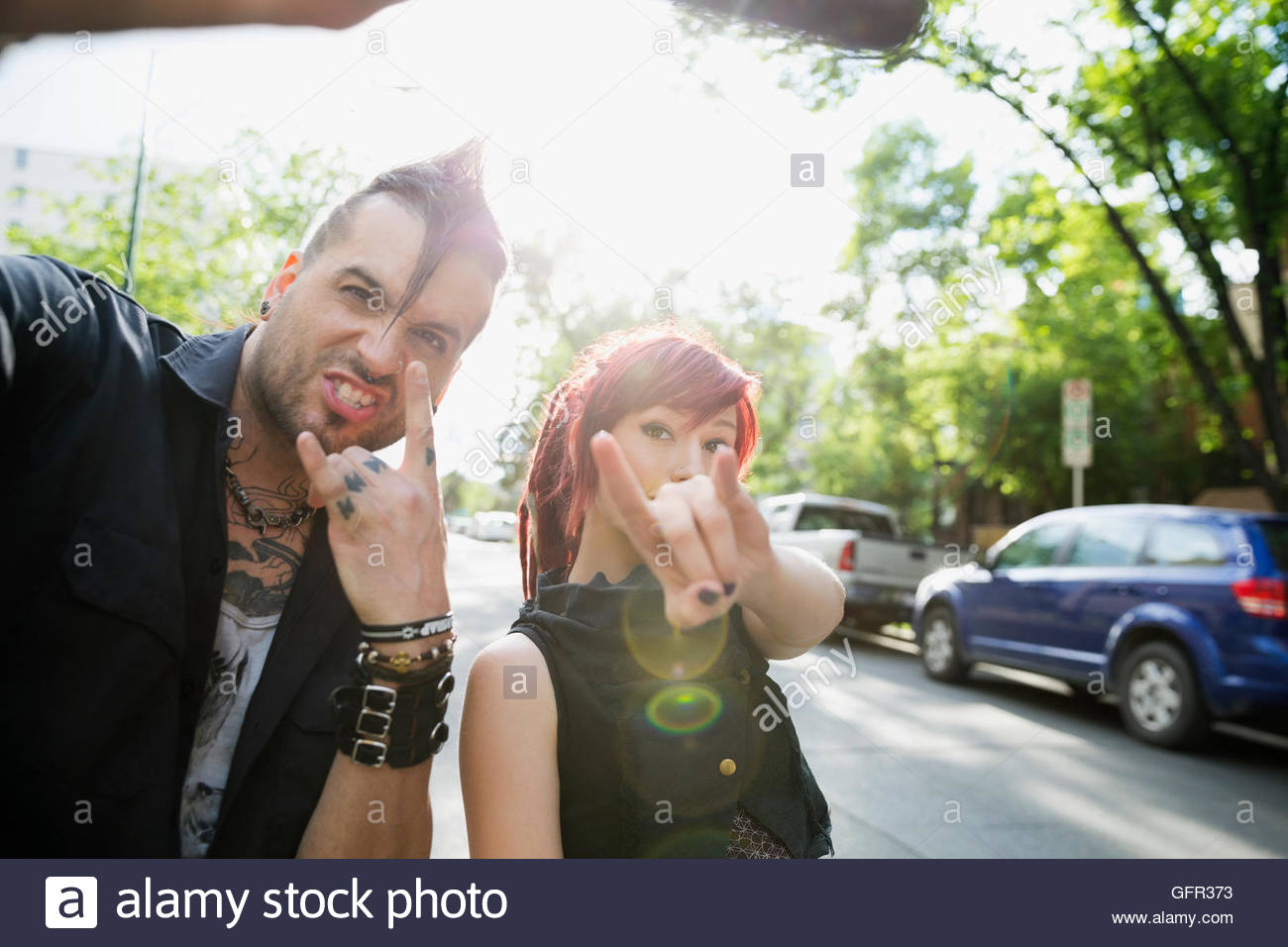 Cool pareja con actitud teniendo selfie gesticulando cuerno firmar en calle Foto de stock