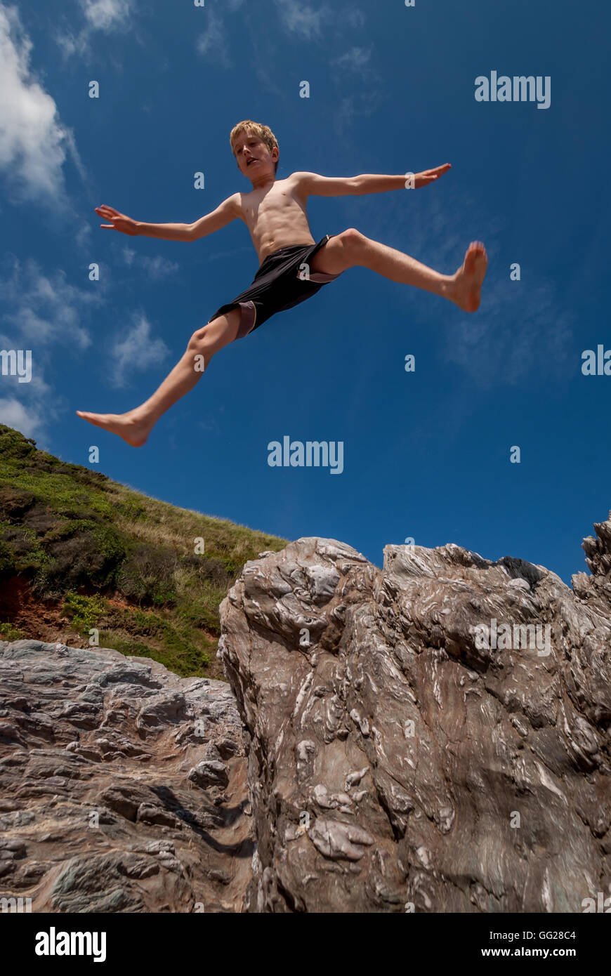 Un muchacho saltando de roca en la playa en el sur de Devon. Foto de stock