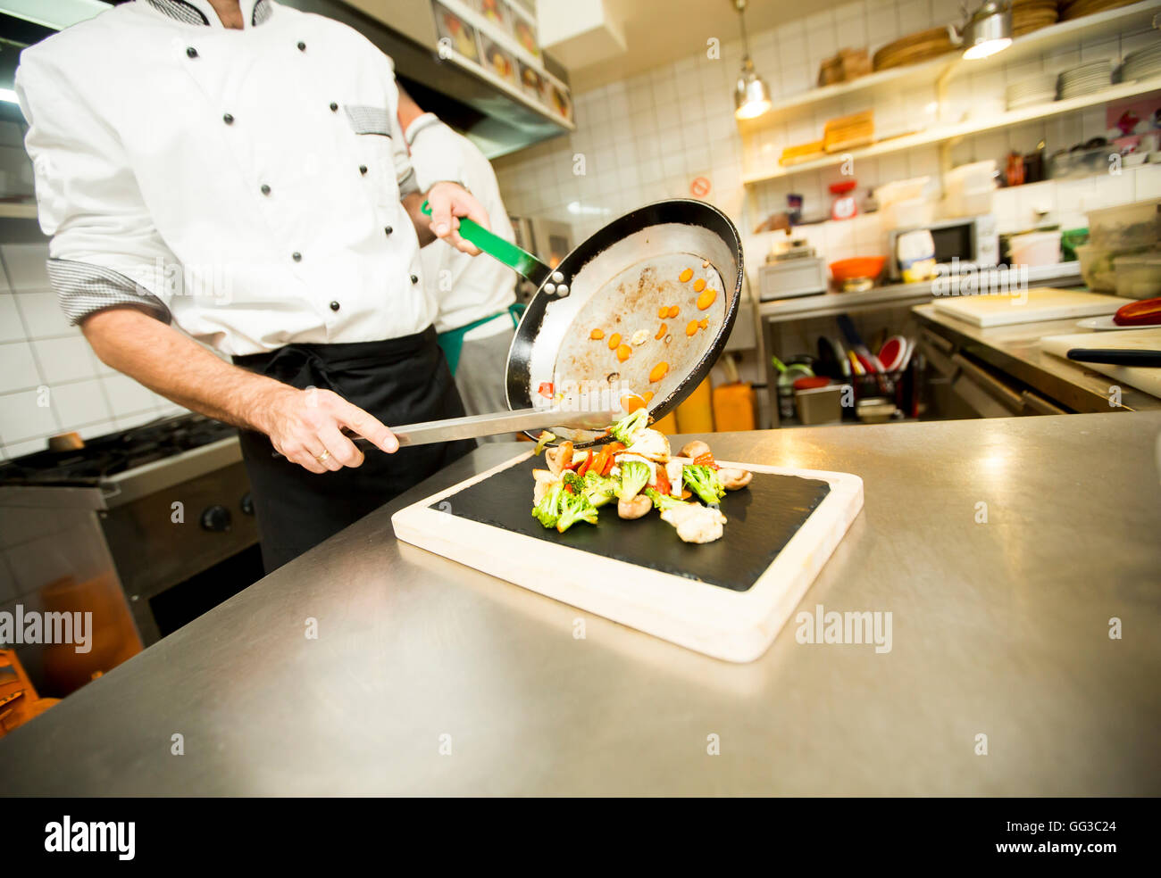 El chef pone a muchas deliciosas verduras en una cacerola en una placa negra Foto de stock
