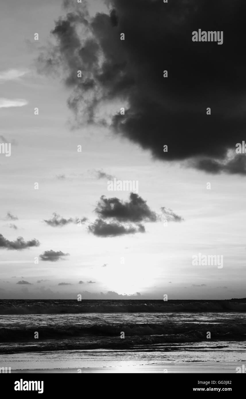 Atardecer en la playa de la mar con nubes y cielo tormenta en penumbra por la luz del sol de tono blanco y negro Foto de stock