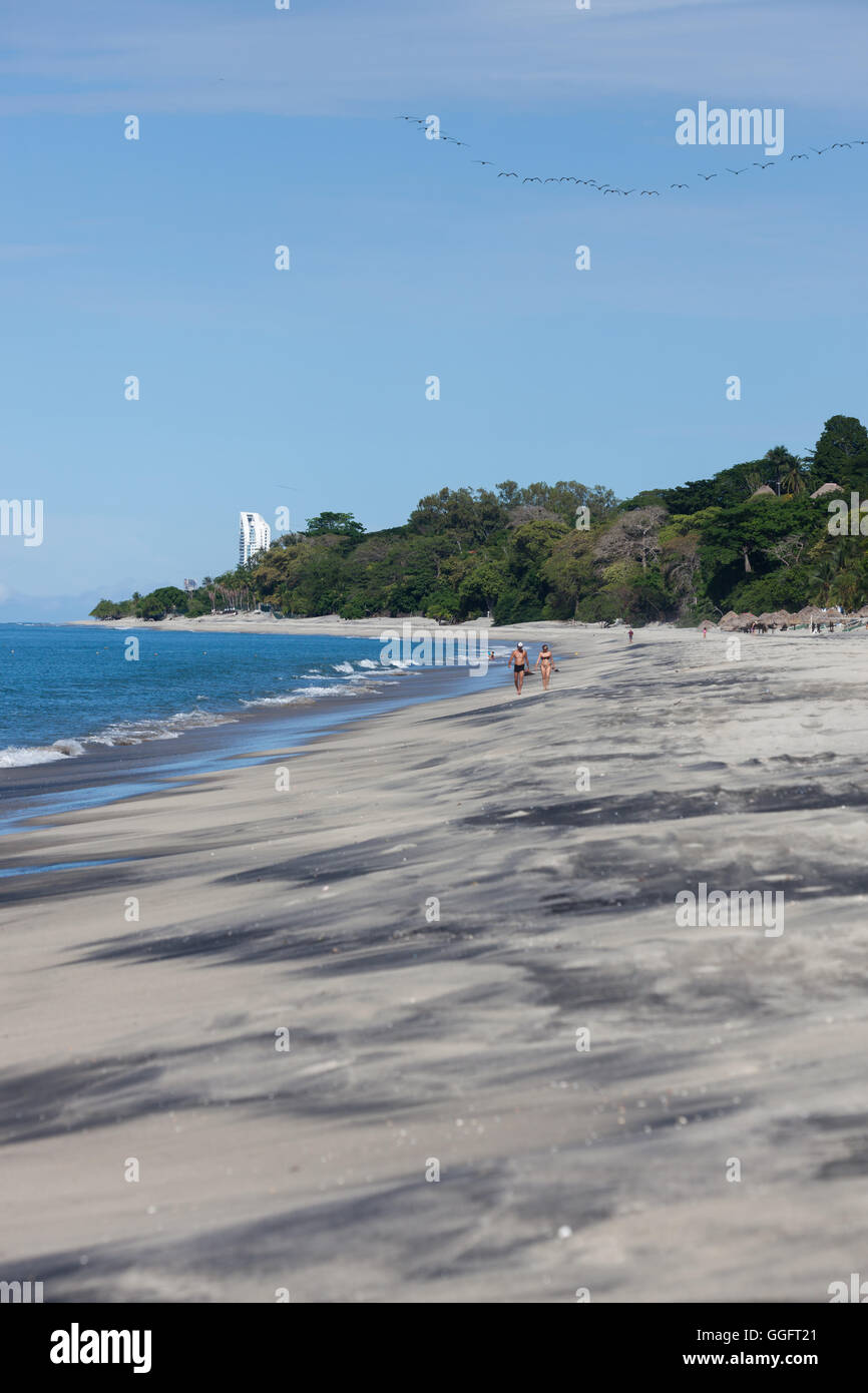 Una escena de playa tropical con olas azules, de mármol negro y marrón arena y gente caminando en Panamá. Foto de stock