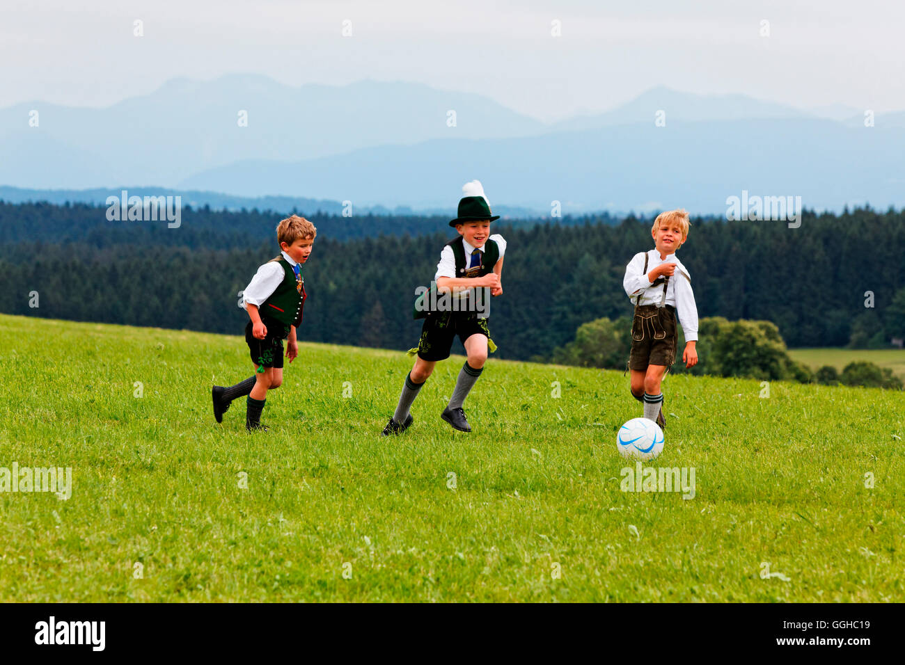 Tres niños en traje tradicional bávaro, jugando al fútbol, Dietramszell Jasberg, Alta Baviera, Baviera, Alemania Foto de stock