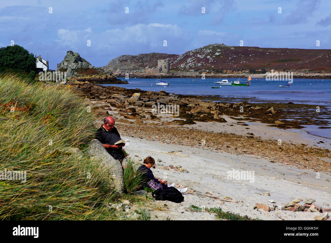 Pareja leyendo en la playa, Anneka's Quay, Bryher, Isles of Scilly, Cornwall, Inglaterra, Gran Bretaña Foto de stock