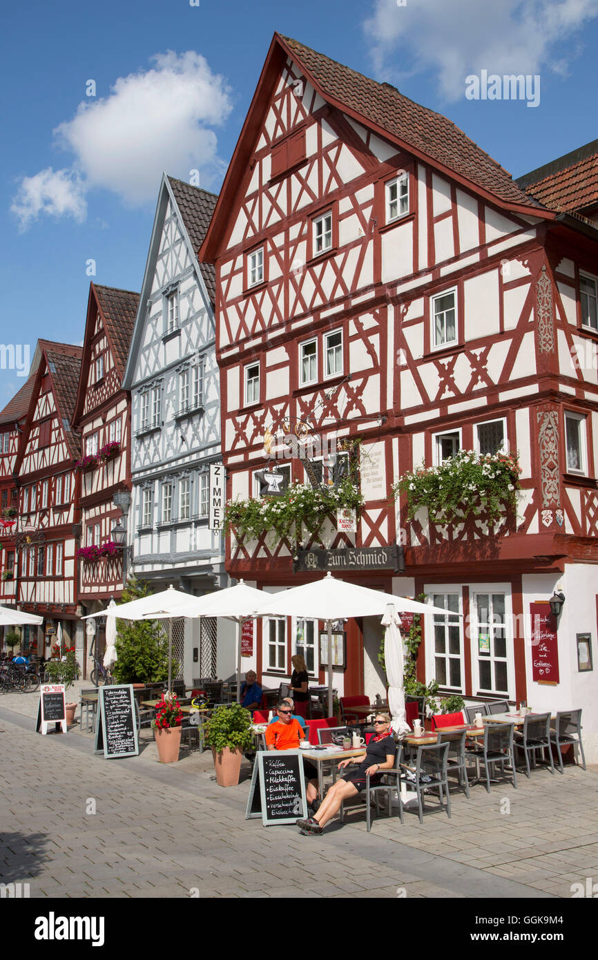 Gente sentada fuera Gasthaus Zum Schmied restaurante cerca de casas con entramados de madera en el casco antiguo de la ciudad, Ochsenfurt, Franconia, Baviera Foto de stock