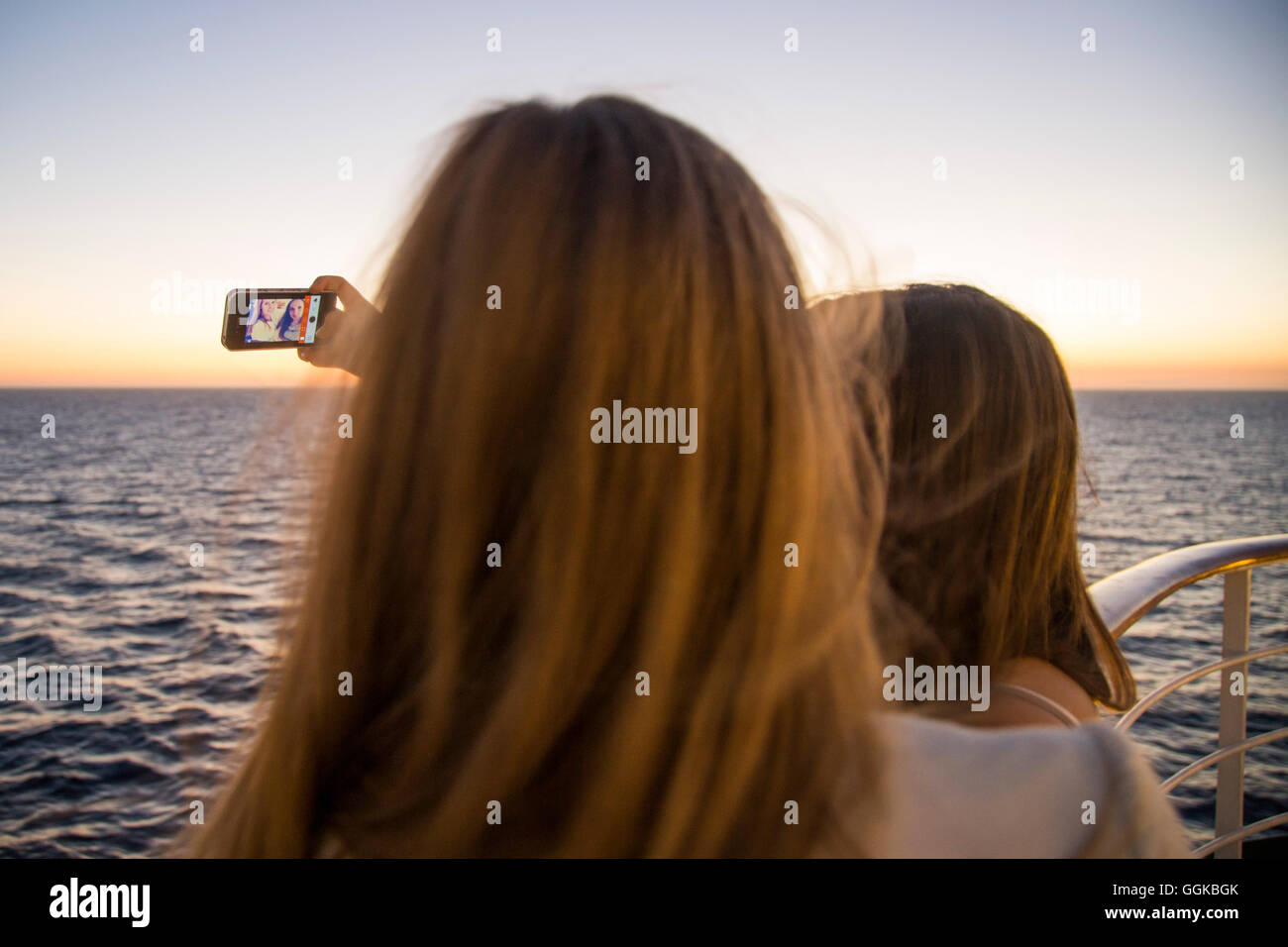 Dos chicas adolescentes tomando una fotografía selfie a bordo del barco crucero MS Deutschland (Peter Deilmann Reederei) al atardecer, Atlantic Oce Foto de stock