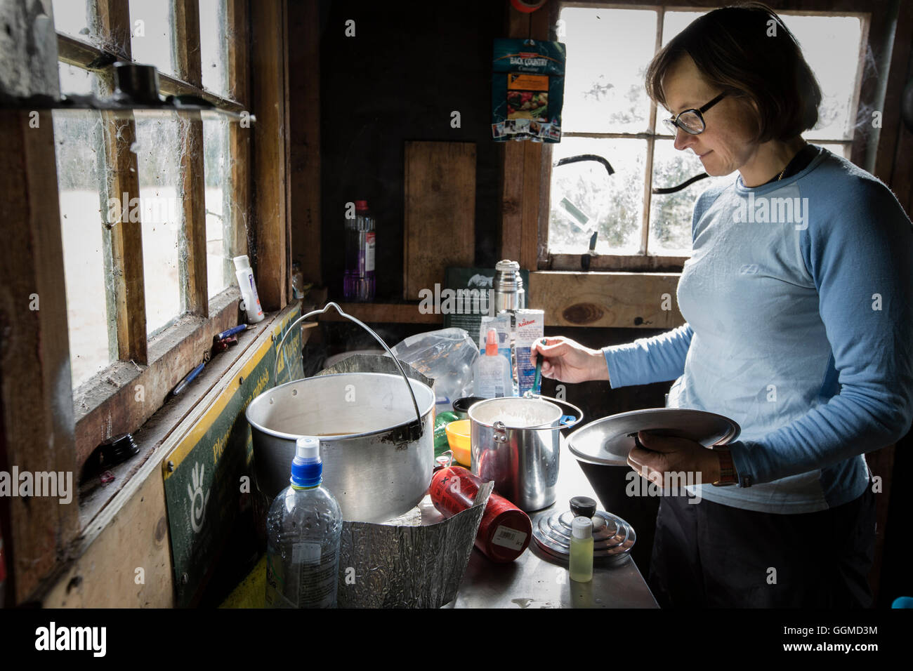 Una mujer cocinando en la desvencijada choza de agua atrás (DOC), Fjordland, lago Manapouri, Isla del Sur, Nueva Zelanda Foto de stock
