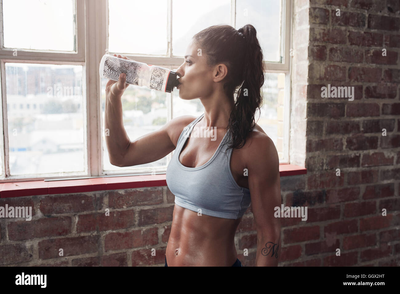 Colocar joven de agua potable en el gimnasio. Mujer toma descanso muscular después del ejercicio. Foto de stock