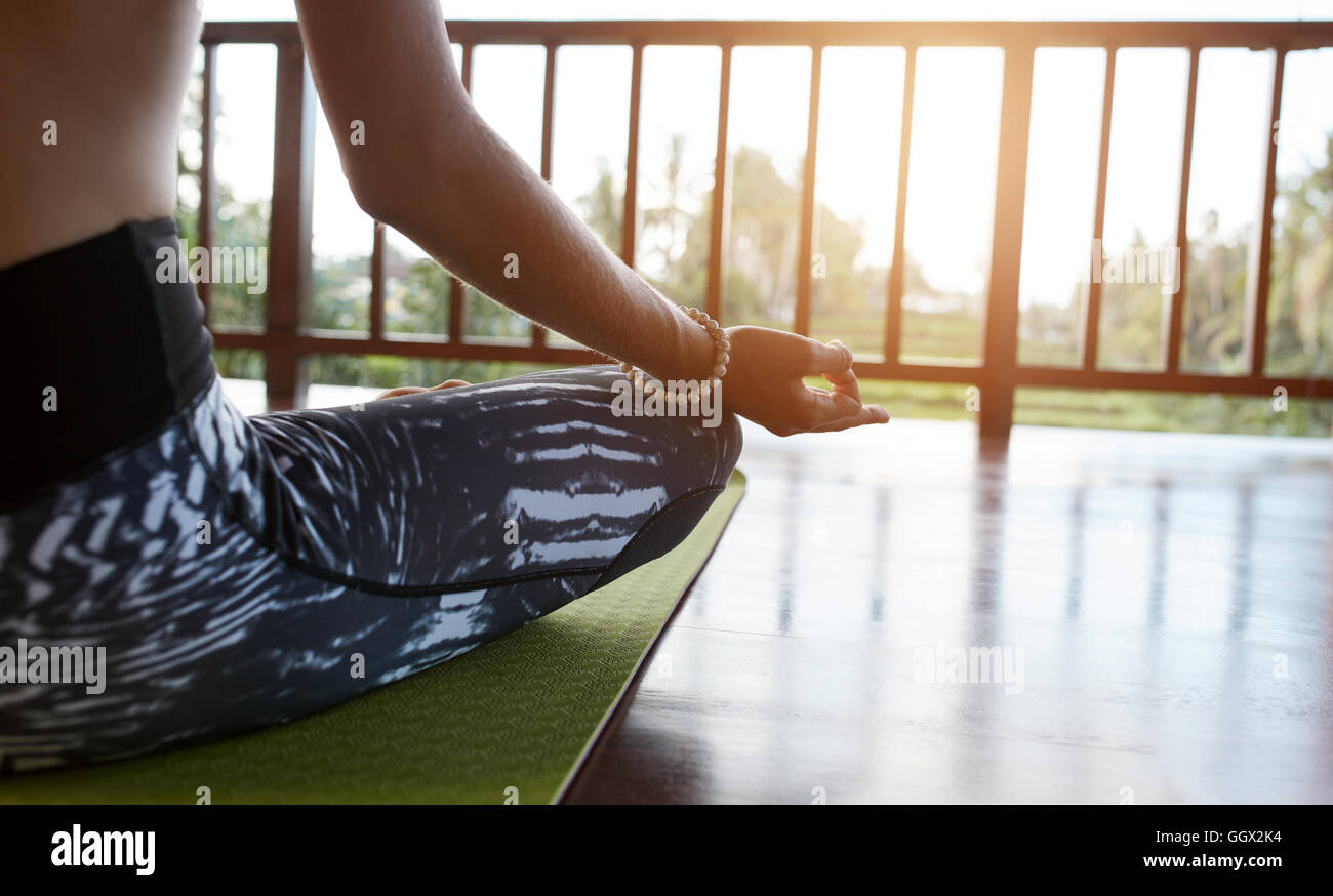 Cerca de la mujer sentada sobre la colchoneta de ejercicios con las piernas cruzadas y las manos sobre las rodillas. Mujer meditando en lotus plantean en clase de yoga, P Foto de stock