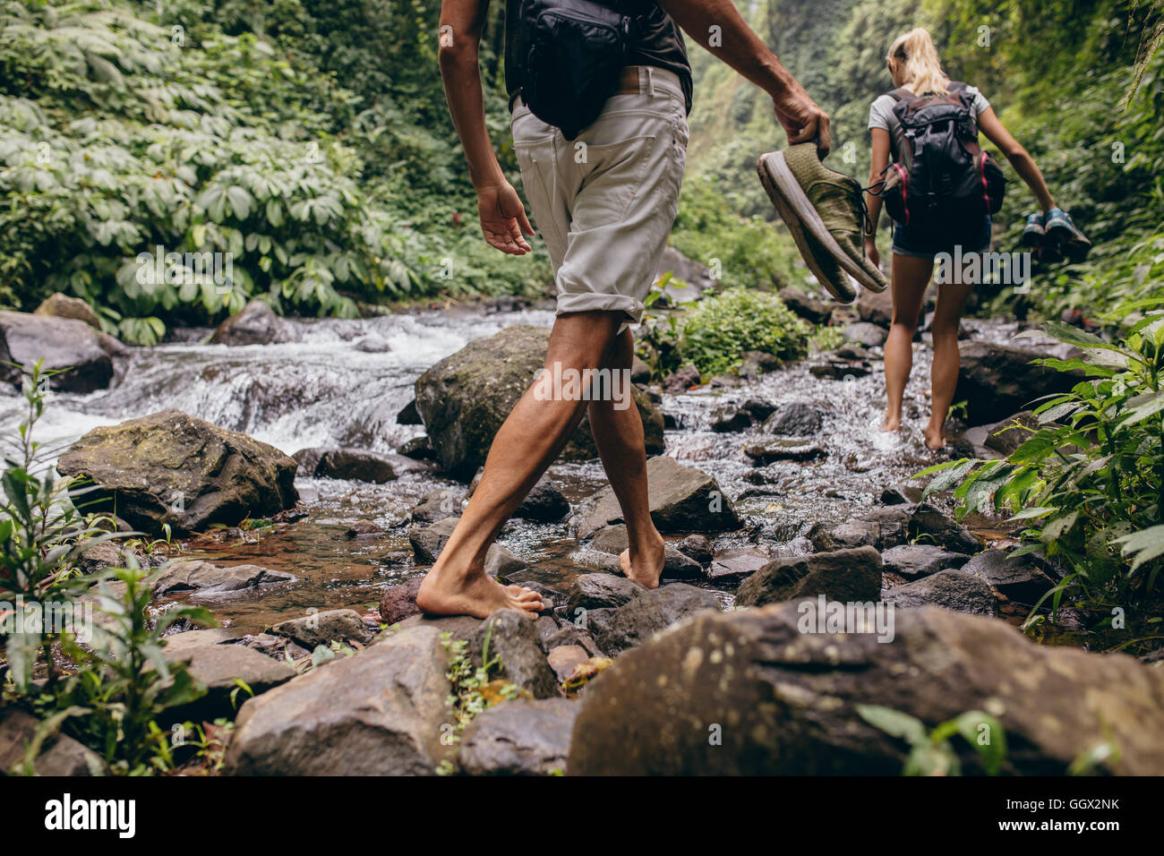 Bajo la sección foto de hombre y mujer cruzar el arroyo descalzas. Pareja paseando por el Creek, en el bosque con sus zapatos en la mano Foto de stock
