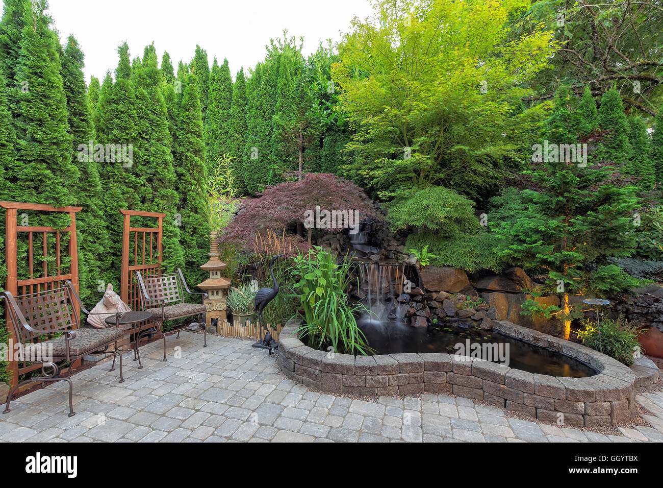 Patio jardín parquizado con cascada estanque plantas árboles enrejado decoración muebles de patio calles de ladrillos Foto de stock