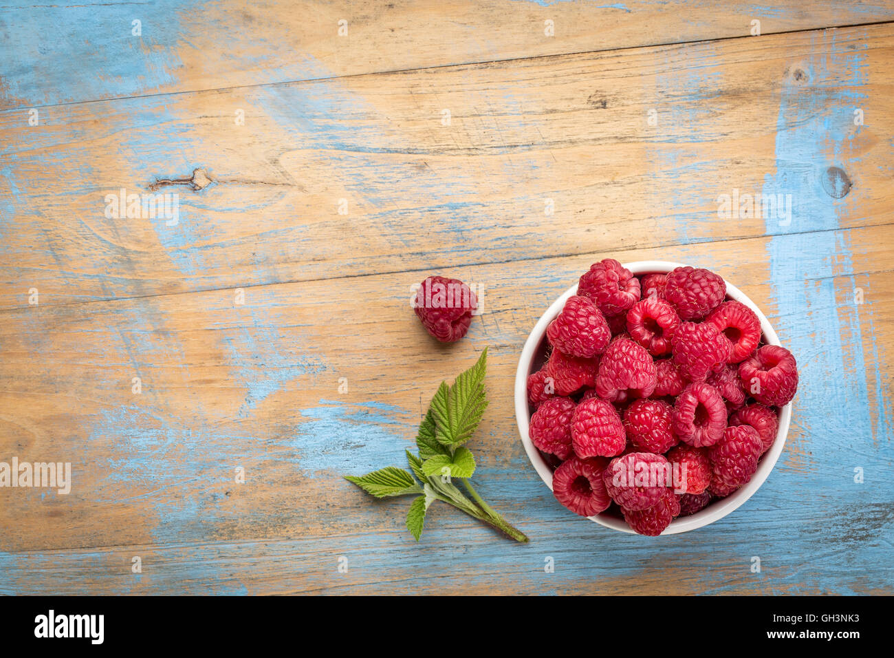 Un tazón de frambuesas rojas frescas en un jardín de madera con un espacio de copia Foto de stock