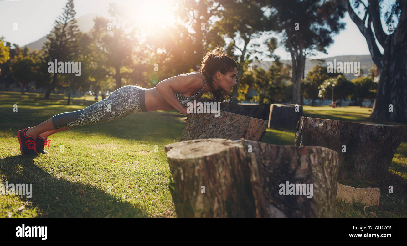 Mujer joven haciendo pushups difíciles en un registro en el parque. Disparo horizontal de un monte joven atleta femenina ejerza en la naturaleza. Foto de stock