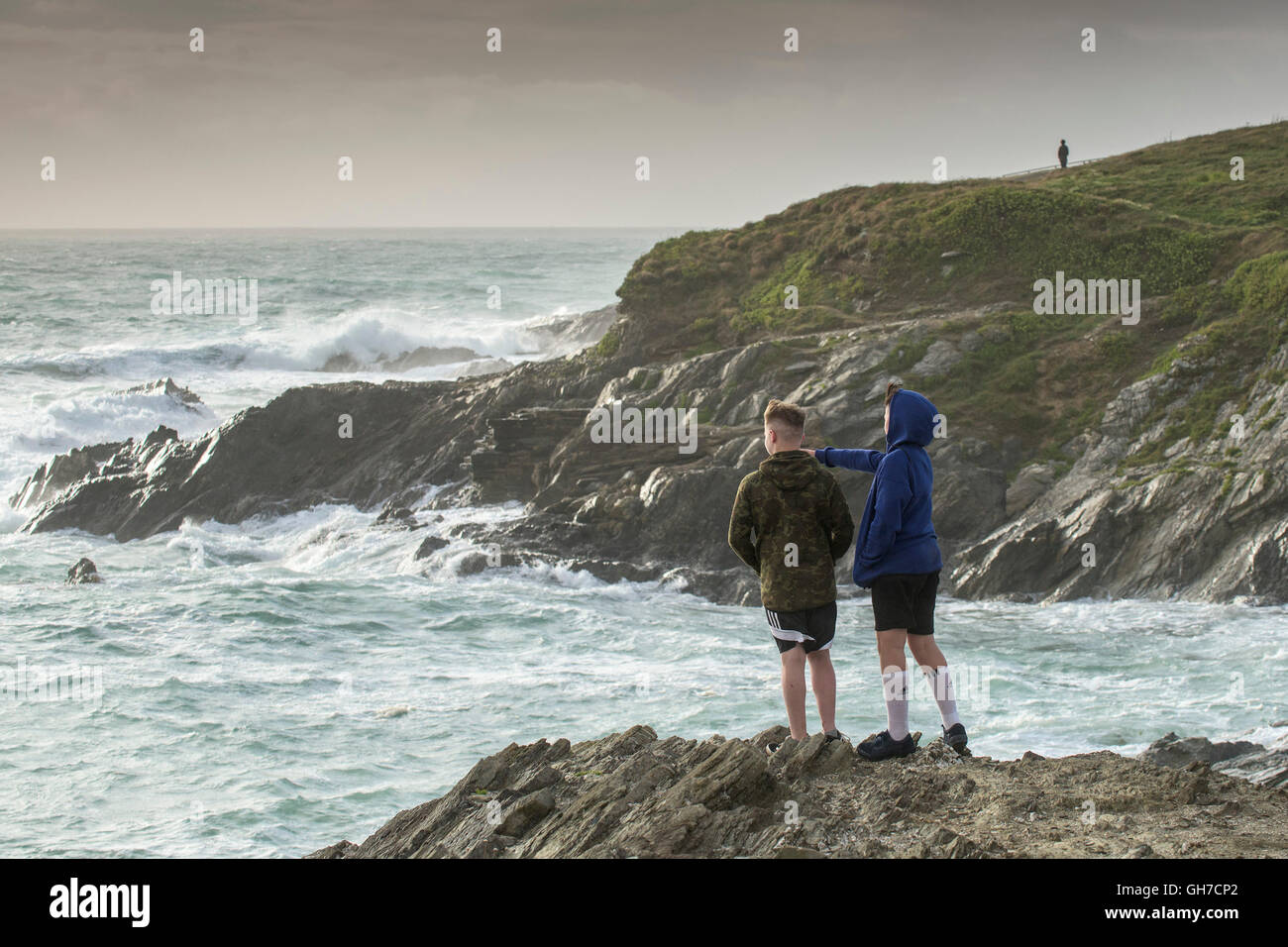 Dos chicos ver el mar estrellarse contra las rocas en Towan cabecero en Newquay, Cornwall. Foto de stock