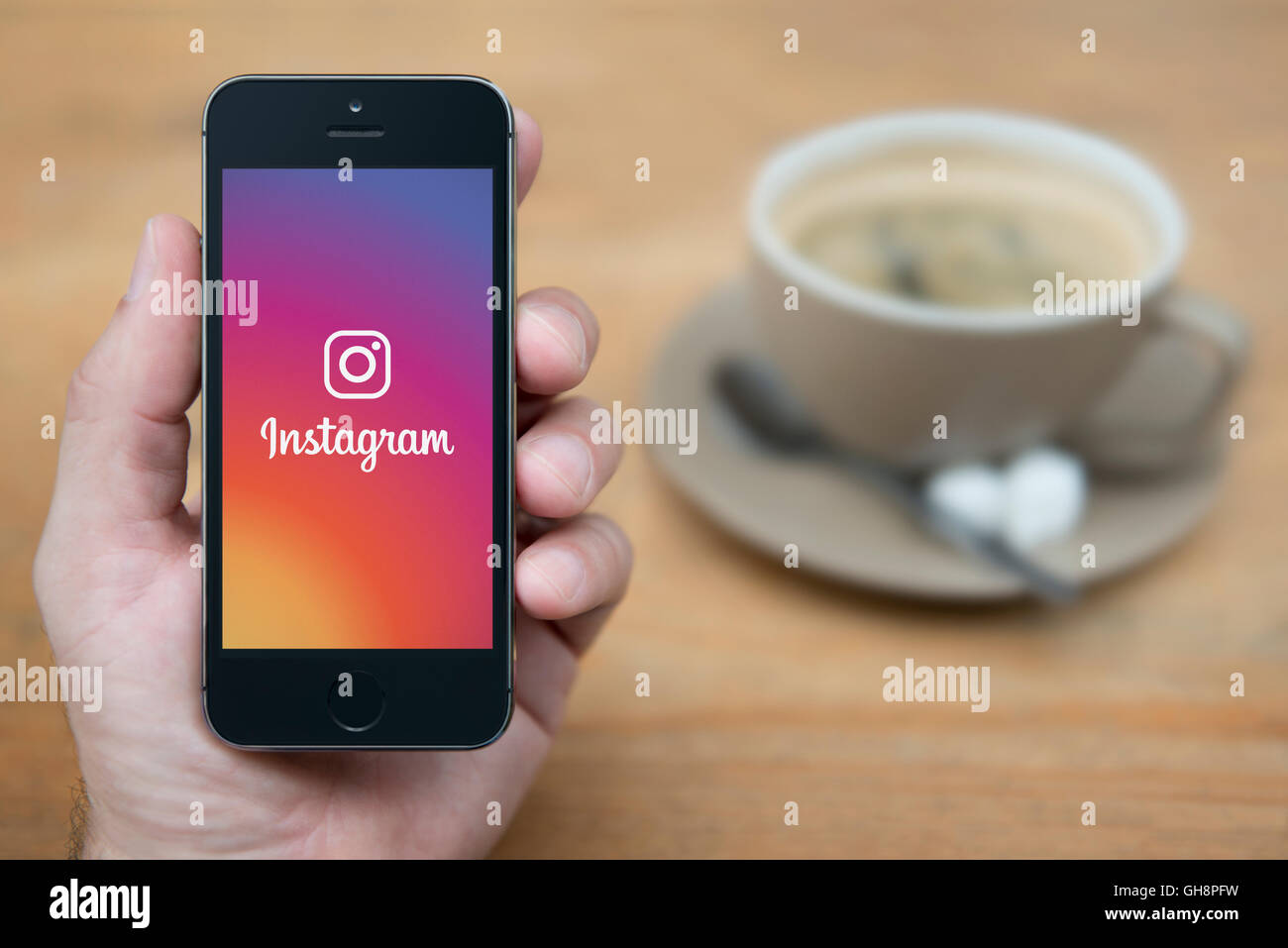 Un hombre mira el iPhone que muestra el logotipo de Instagram, una vez sentado, con una taza de café (uso Editorial solamente). Foto de stock