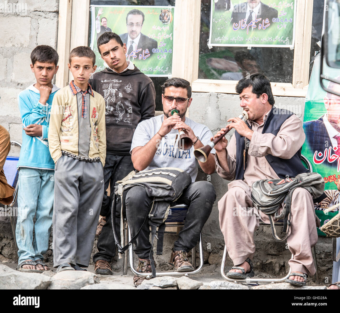 Tubos de músicos tocando en Karimabad.en el norte de Pakistán. Están sentados en sillas y vigilados por una pequeña multitud. Foto de stock