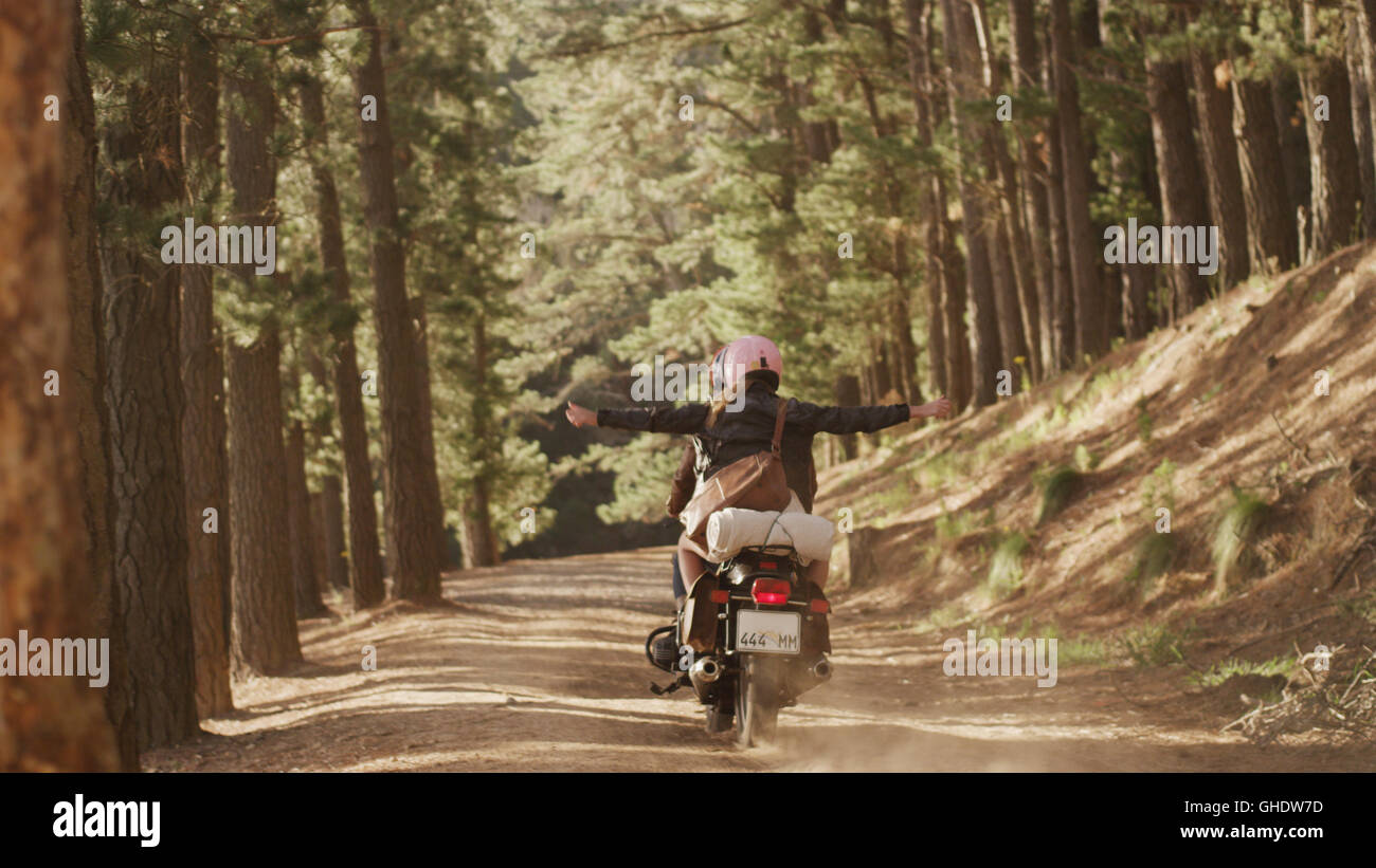 Una exuberante jovencita montando moto por camino de tierra en los bosques Foto de stock