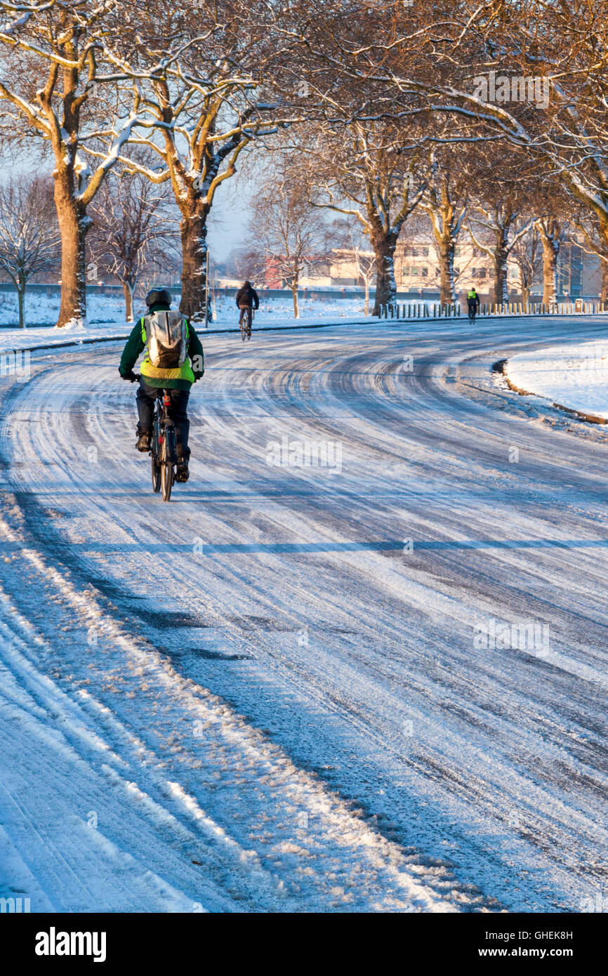Ciclismo ciclista en una carretera cubierta de hielo y nieve en invierno con otros ciclistas en la distancia, Nottingham, Inglaterra, Reino Unido. Foto de stock