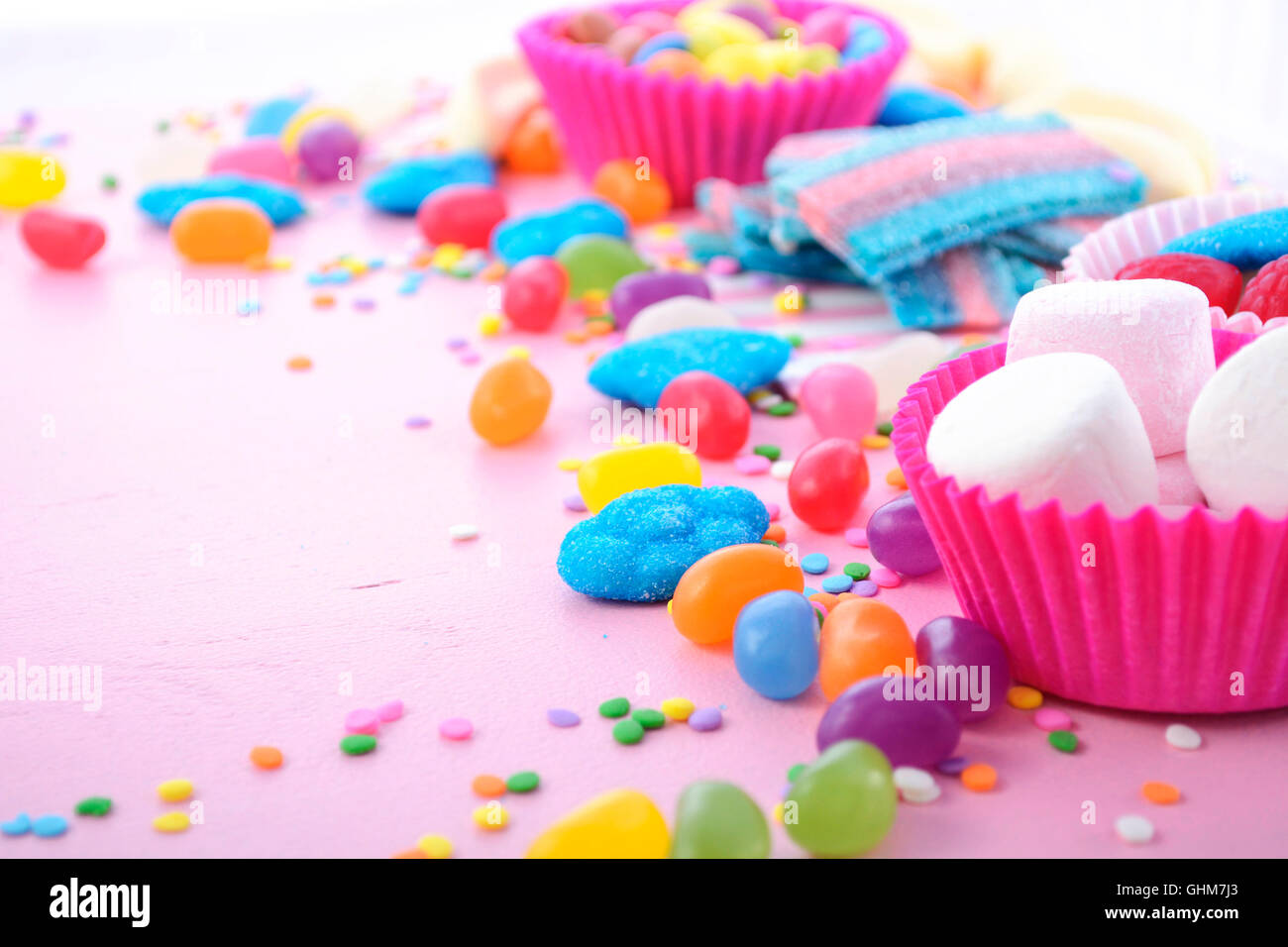 Caramelos de colores brillantes sobre fondo rosa mesa de madera para Halloween truco de tratar o cumpleaños infantiles cotillón, closeup. Foto de stock