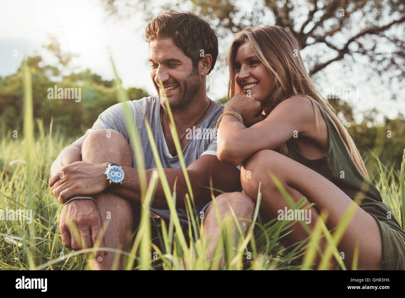 Retrato de pareja joven sonriente en el amor sentados juntos al aire libre en el campo. Feliz el hombre y la mujer joven en la pradera. Foto de stock