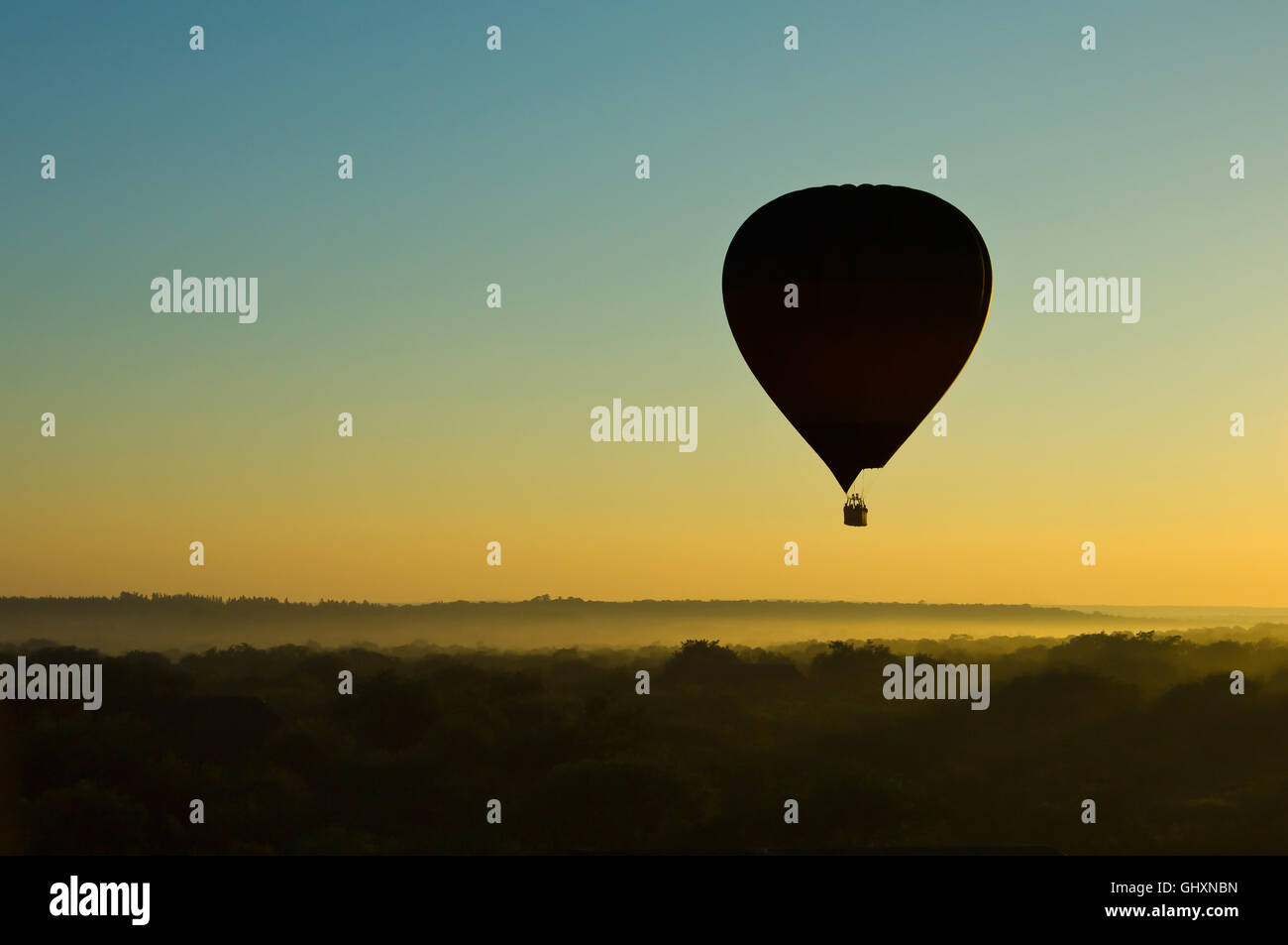 Silueta de un globo de aire caliente en un cielo despejado al amanecer sobre Misty llanura africana Foto de stock