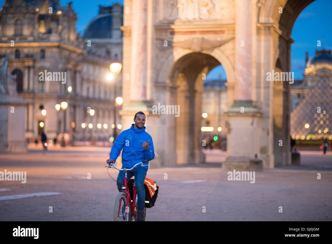 Un ciclista pasando el Arc de triomphe du Carrousel & Palais du Louvre al atardecer, París, Francia Foto de stock