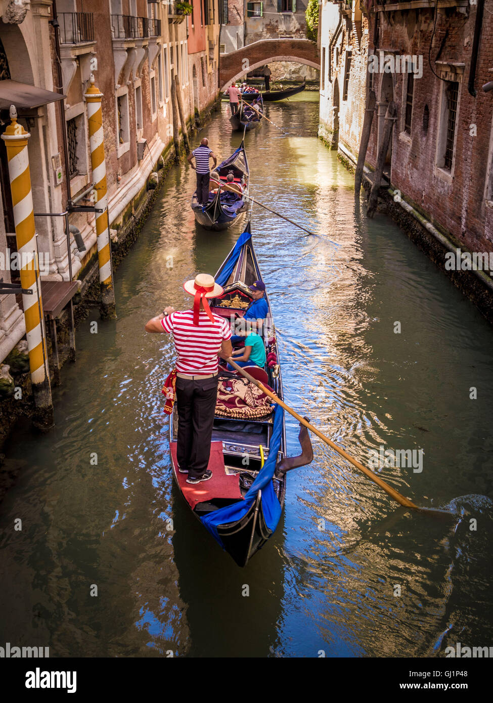 Gondolero vistiendo tradicionales top de rayas y navegante hat su dirección en góndola por un estrecho canal de Venecia, Italia. Foto de stock