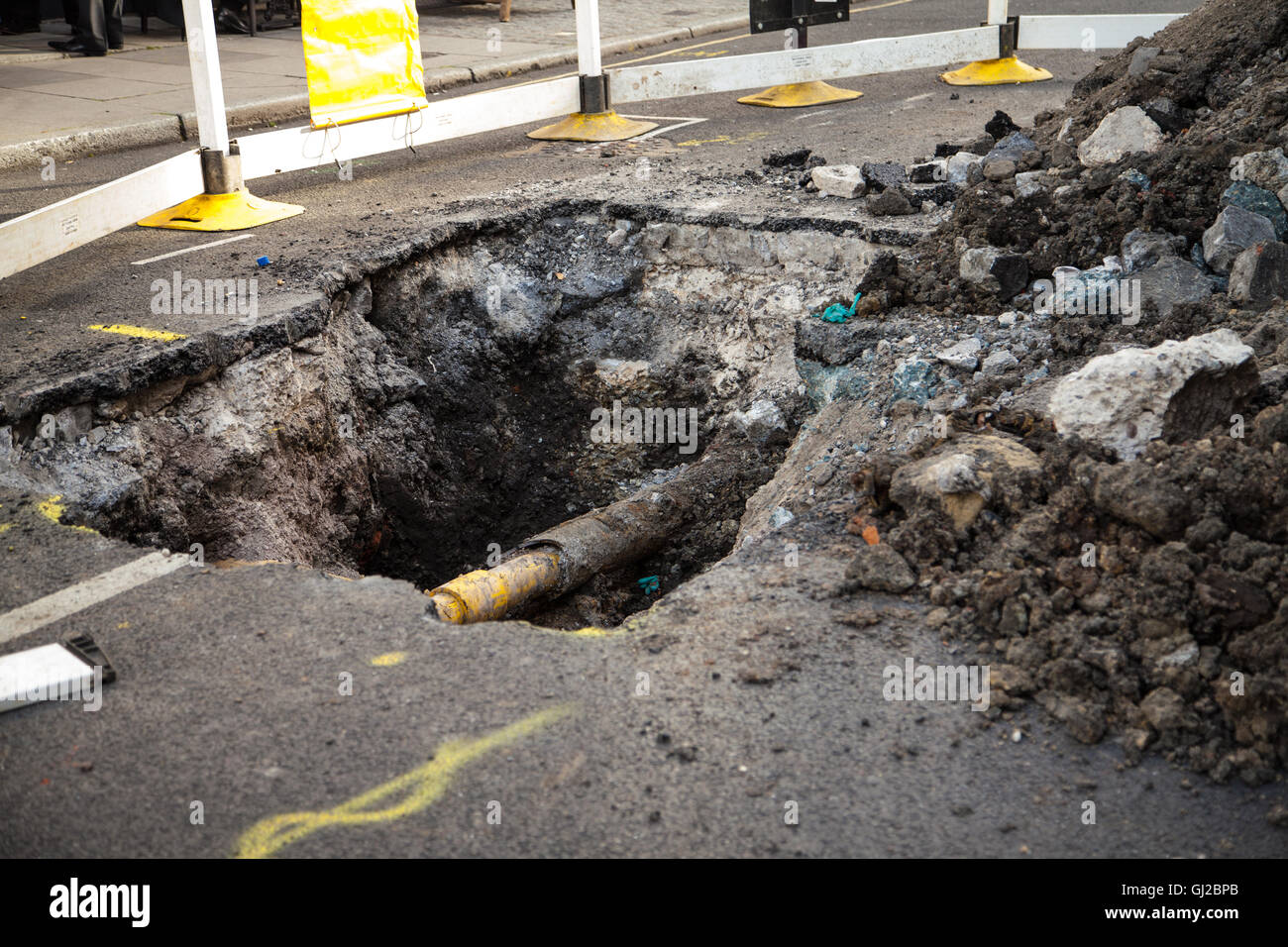 Un agujero en la calle, revelando un tubo amarillo en una obra de construcción en Camden, Londres 2016. Los escombros y restos en el lateral. Foto de stock