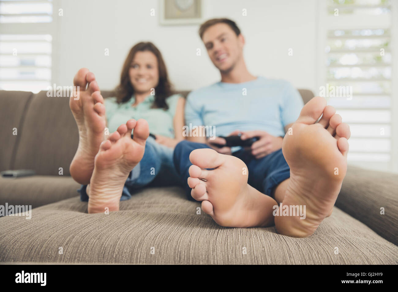 Par descalzo sobre el sofá con video game controller Foto de stock