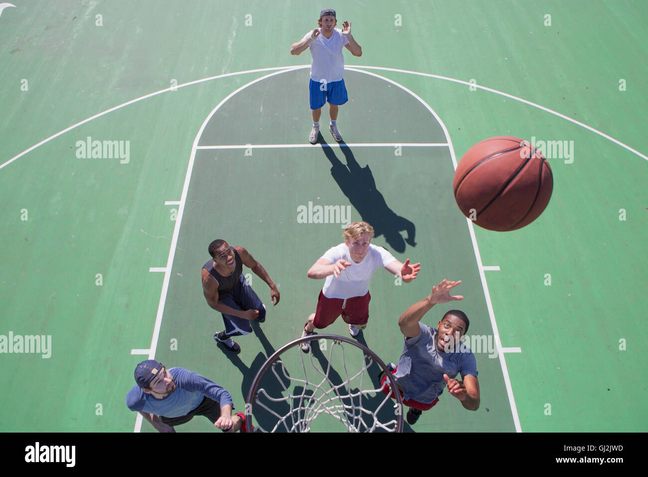 Grupo de amigos varones jugando baloncesto en la corte exterior, niveles elevados de ver Foto de stock