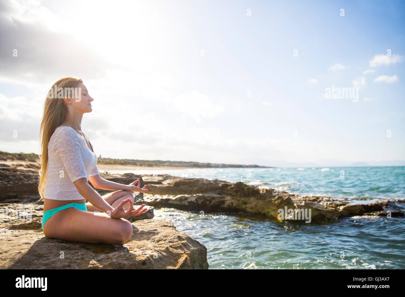 Mujer joven sentada sobre las rocas por el mar, en posición de yoga Foto de stock
