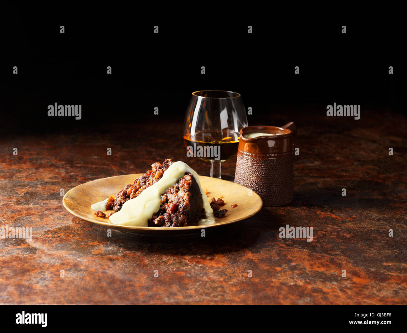De vainilla y salsa de Armagnac vertida sobre el pudín de Navidad, una copa de brandy y el bote de salsa Foto de stock