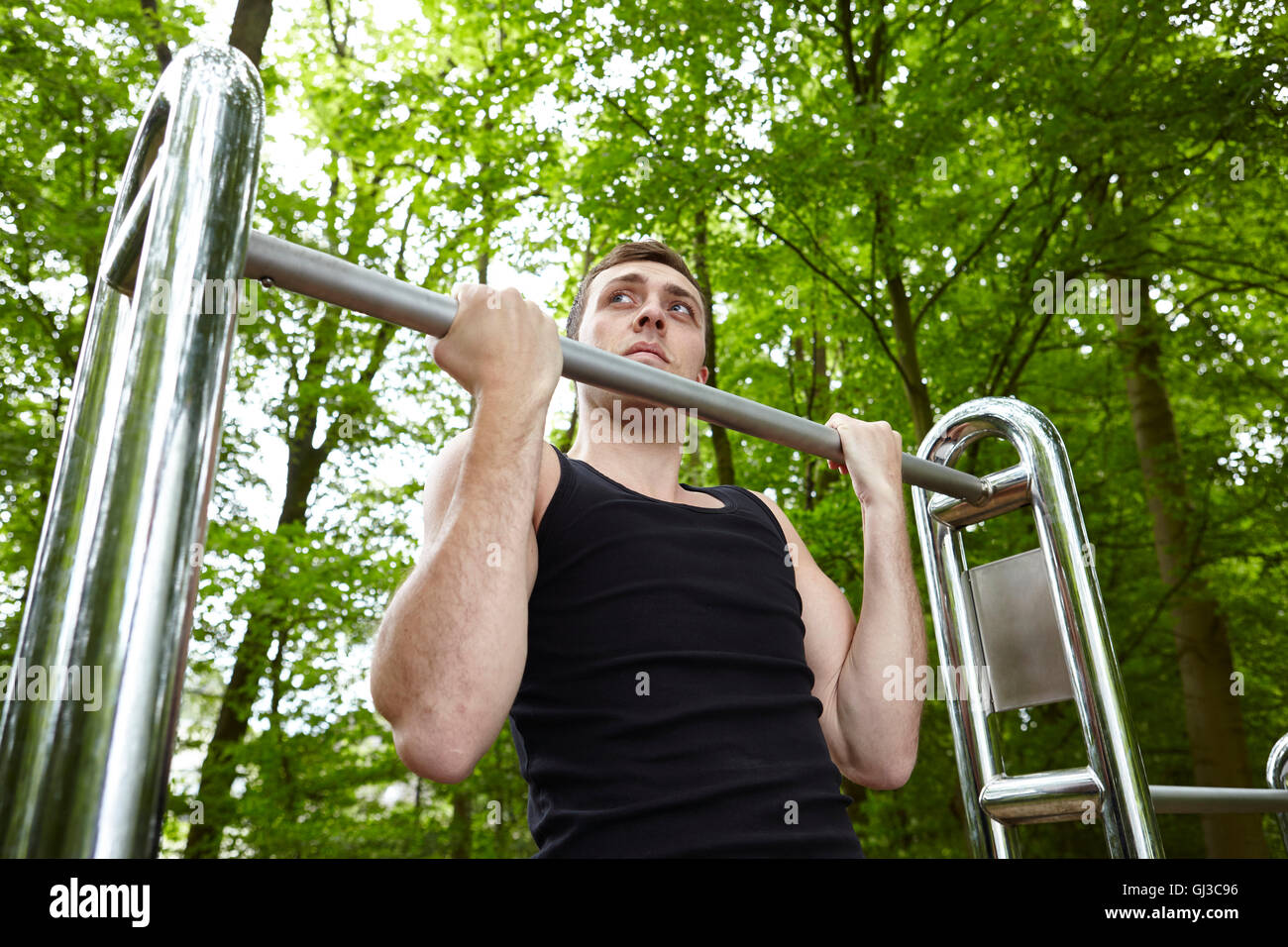 Joven formación en park, haciendo chin ups en ejercicio bares Foto de stock