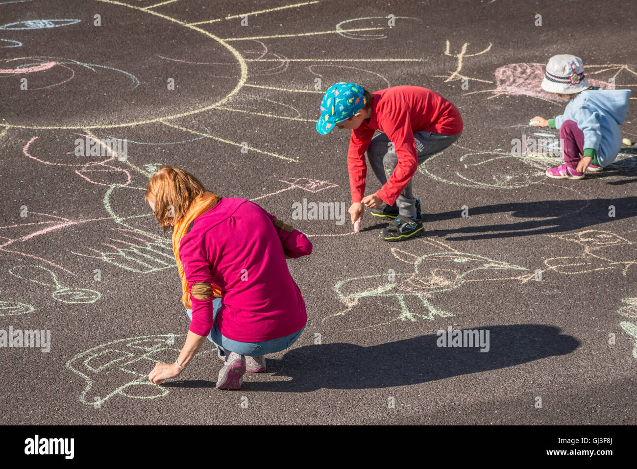 Madre caucásica jugando con dos niños dibujando figuras con tiza en actividades al aire libre familiares de asfalto. Foto de stock