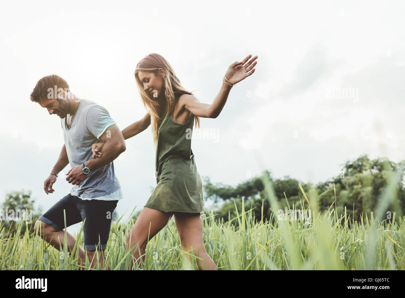 Disparó al aire libre de la joven pareja caminando por los prados de la mano. Hombre y mujer hablando a pie a través de campo de hierba en el campo. Foto de stock