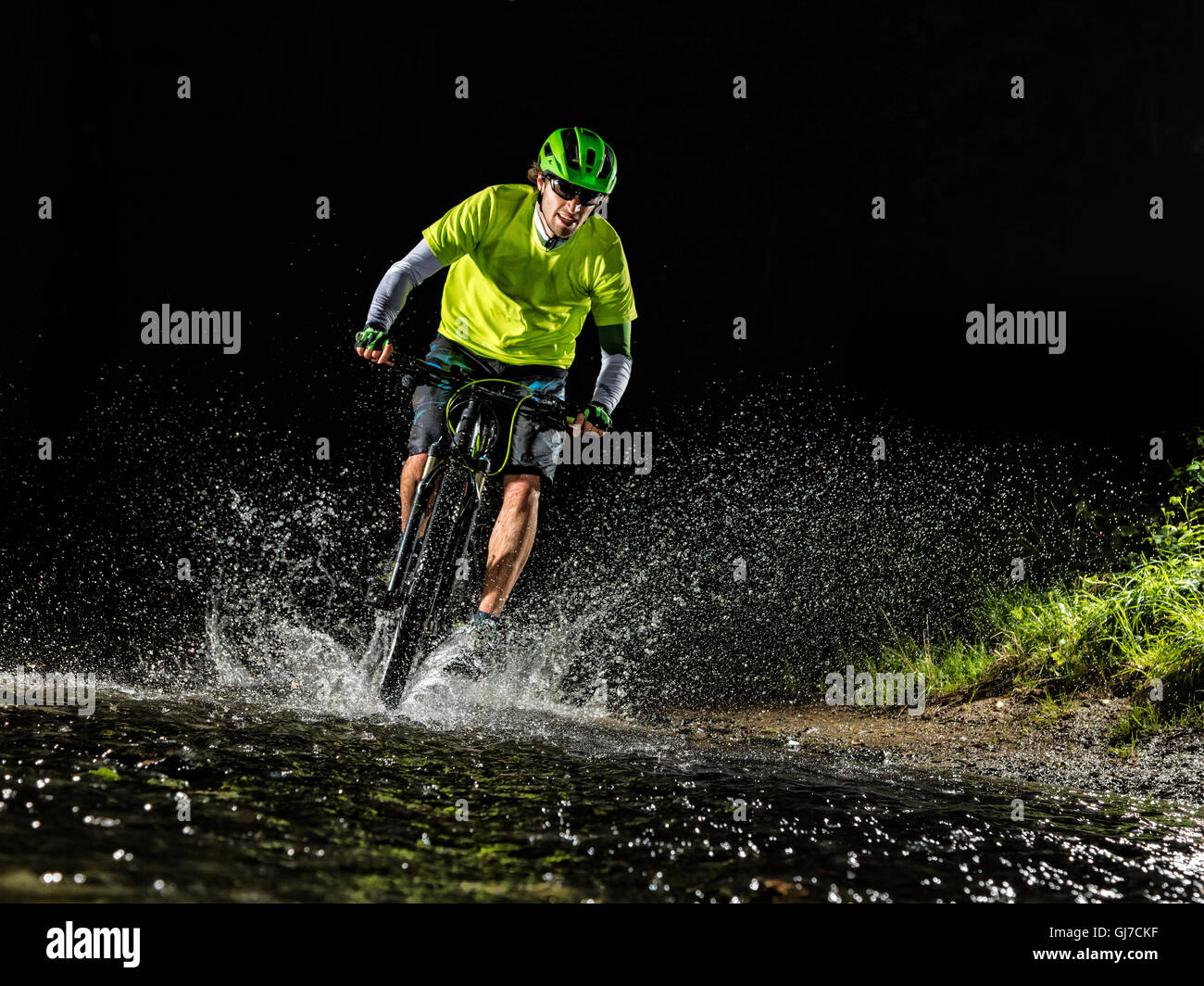 Ciclista de montaña equitación en forest stream, en torno a las salpicaduras de agua. Foto de stock