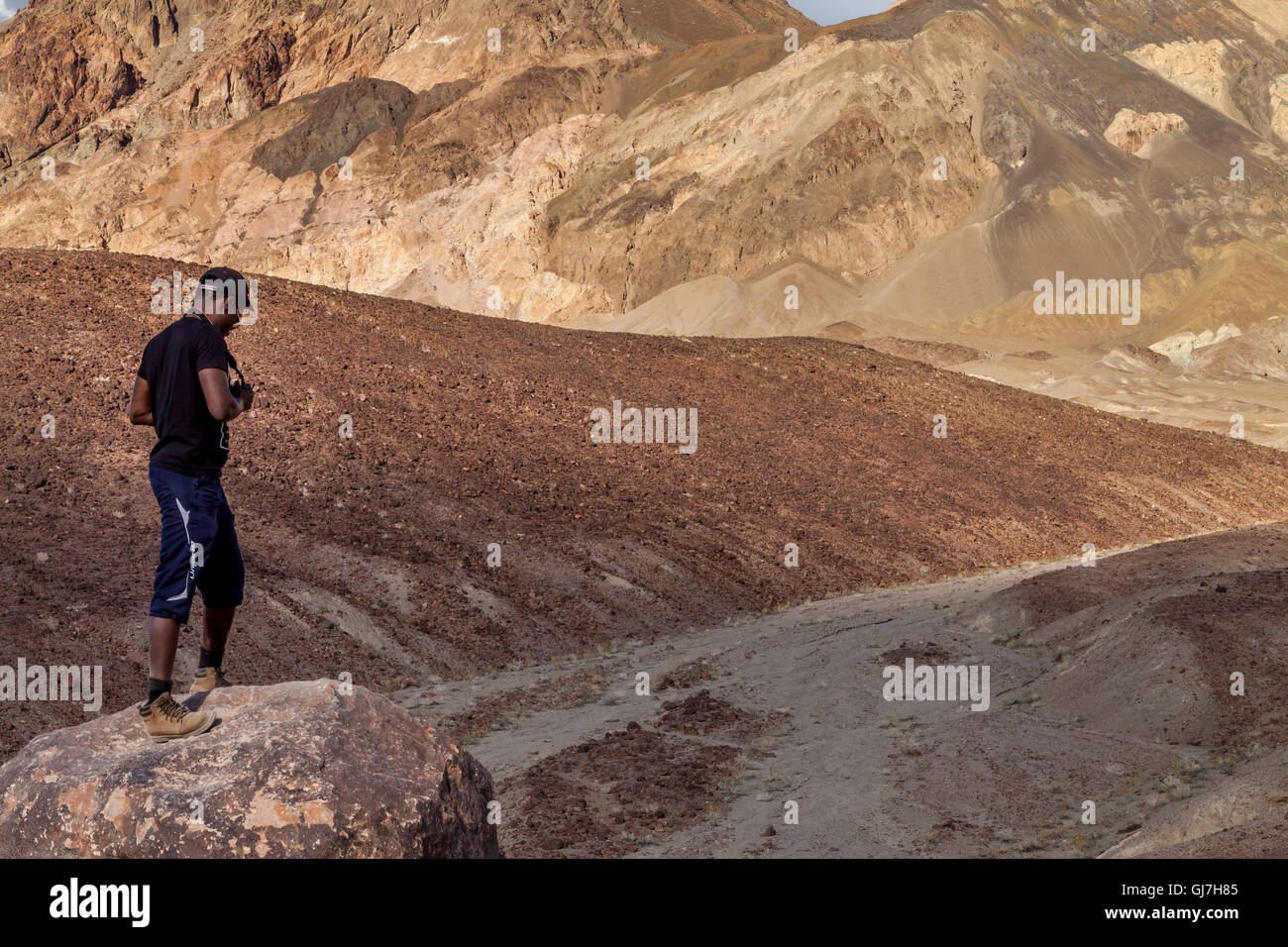 Macho negro turista tomando fotos de las colinas volcánicas y sedimentarias cerca de paleta del artista en el Parque Nacional Valle de la muerte, Ca Foto de stock