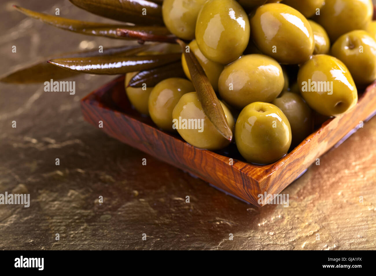 Aceitunas verdes en el plato de madera sobre un fondo de oro Foto de stock