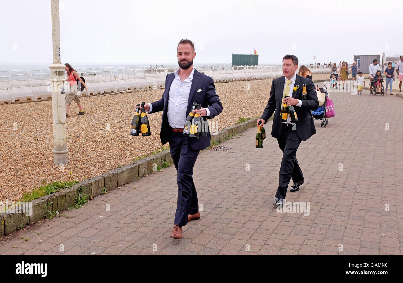 Los invitados a la boda en el quiosco Brighton Seafront portando botellas de vino espumoso prosecco. Foto de stock